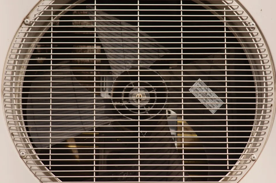 Outdoor air conditioner fan behind a metal grille.
