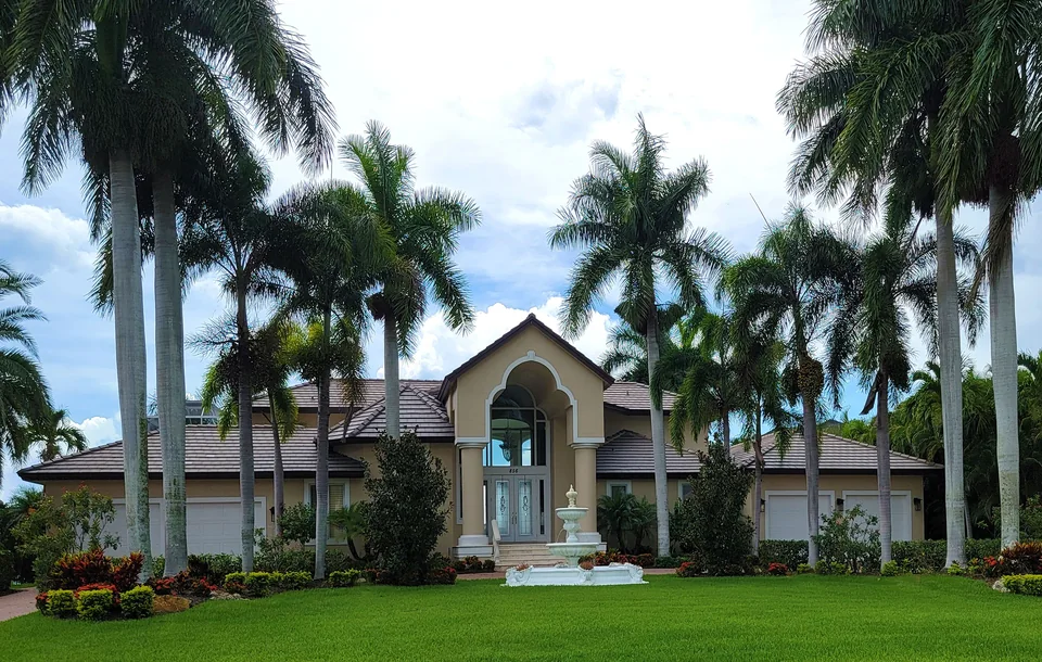 Tropical house with a tiled roof, lawn and palm trees.