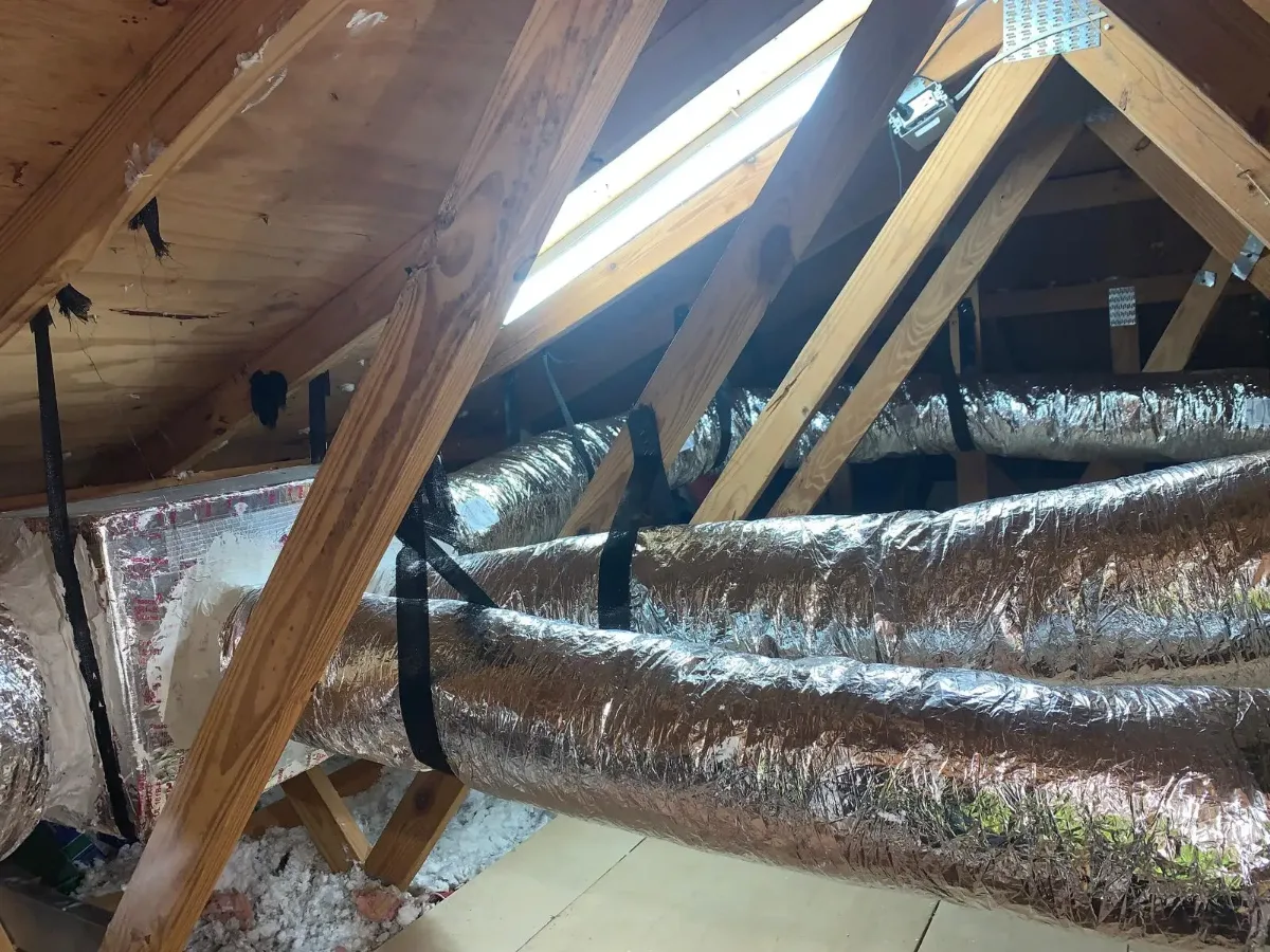 Insulated air ducts beneath wooden attic rafters.