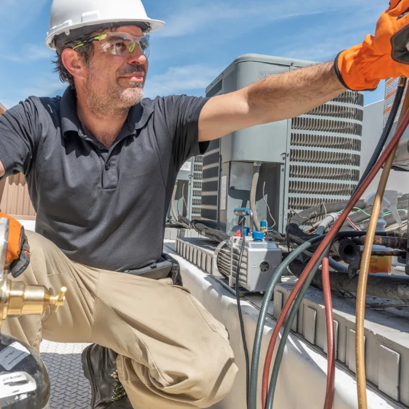 Technician beside rooftop air conditioning equipment.