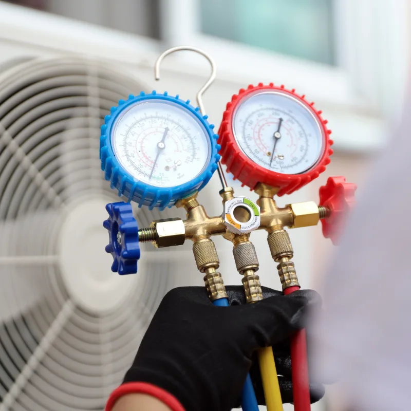 Blue and red refrigerant pressure gauges beside an air conditioner.