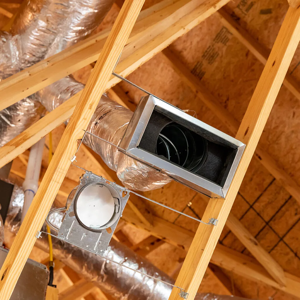 Insulated air ducts running between wooden attic trusses.