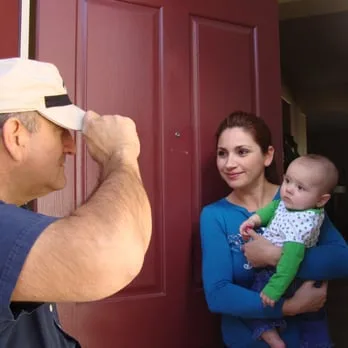 Worker greeting a homeowner and child at a front door.